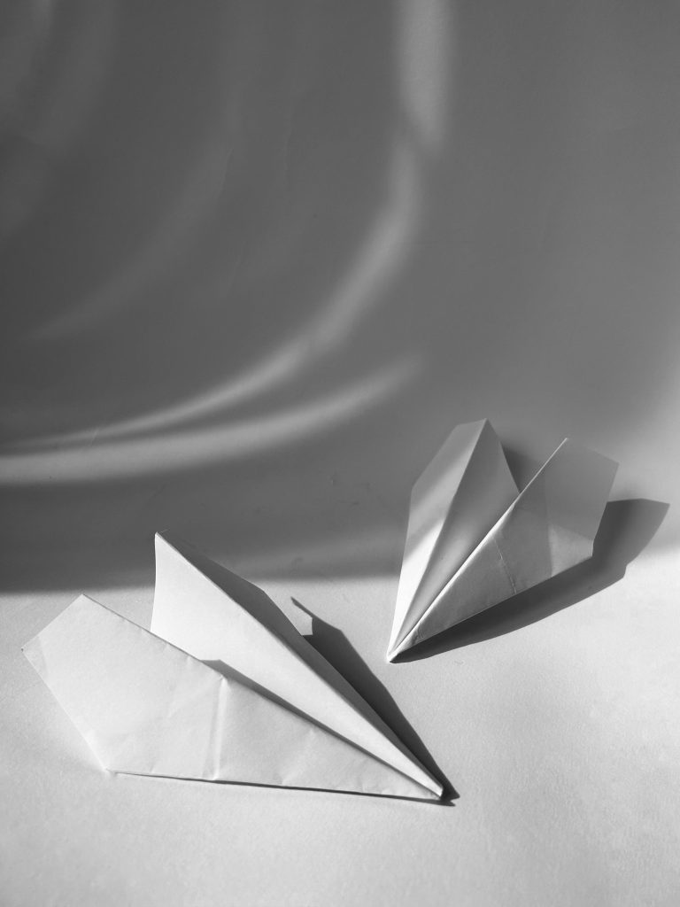 Artistic black and white photo featuring two folded origami paper airplanes with dramatic shadows.