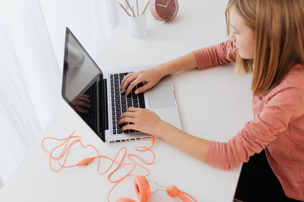 Teenage girl focused on laptop, wearing headphones, in a modern minimalistic setting.